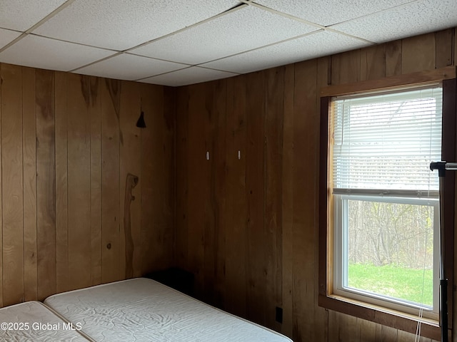 bedroom featuring a drop ceiling and wood walls
