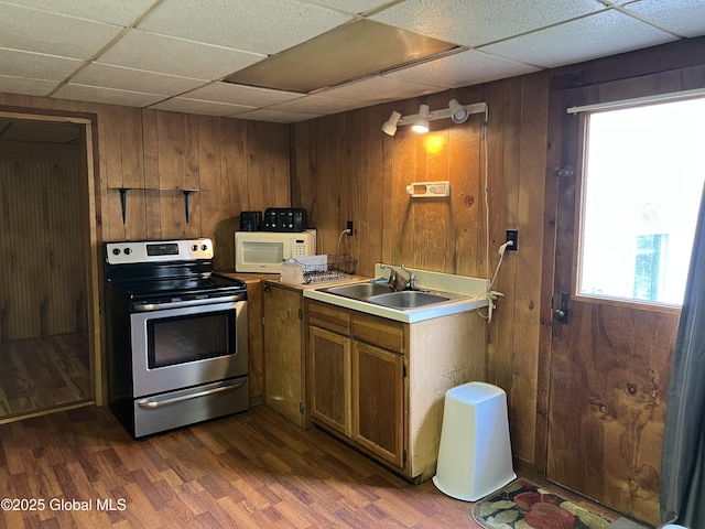kitchen featuring white microwave, wooden walls, dark wood-style floors, a sink, and stainless steel electric range oven