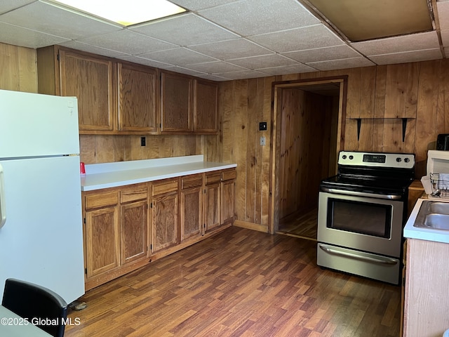 kitchen with dark wood-style flooring, a paneled ceiling, stainless steel range with electric stovetop, freestanding refrigerator, and wooden walls