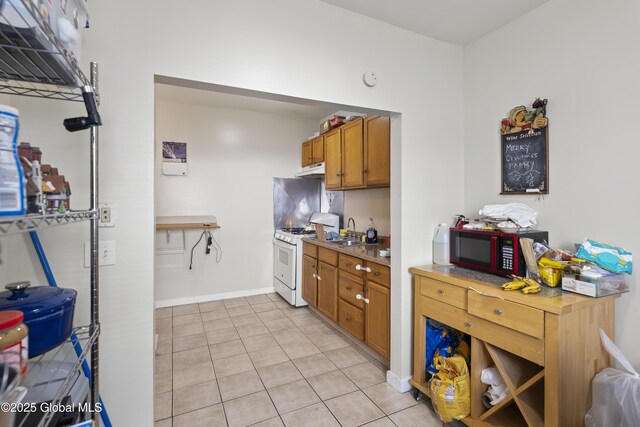 100 3rd St, Waterford, NY 12188 - kitchen with brown cabinetry, light tile patterned flooring, white range with gas stovetop, under cabinet range hood, and a sink