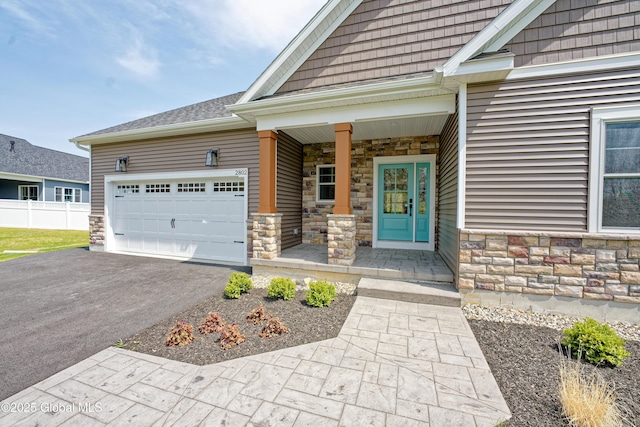 property entrance featuring covered porch, an attached garage, stone siding, and aphalt driveway