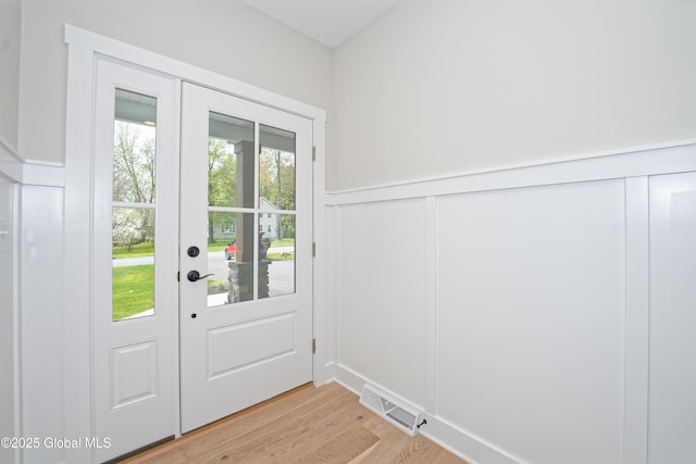 doorway with french doors, visible vents, wainscoting, a decorative wall, and light wood-style flooring
