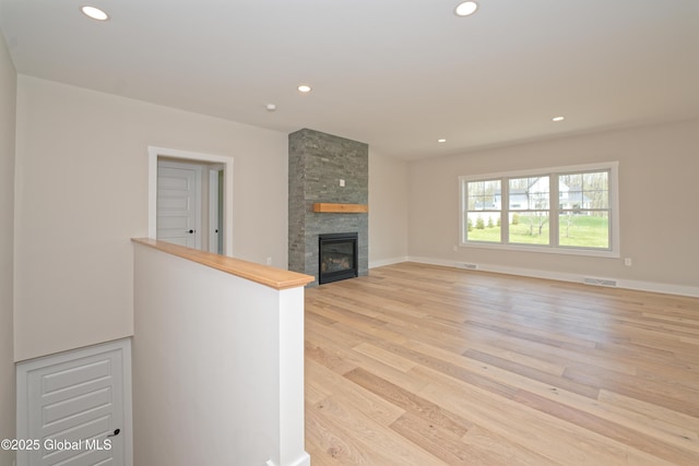 unfurnished living room with a stone fireplace, recessed lighting, baseboards, light wood-type flooring, and visible vents