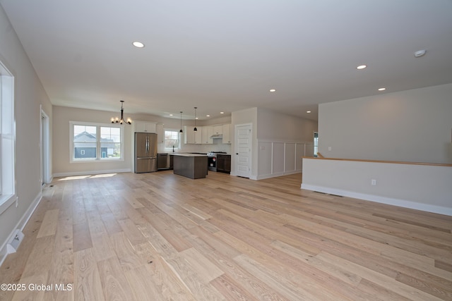 unfurnished living room with an inviting chandelier, recessed lighting, a sink, and light wood-type flooring