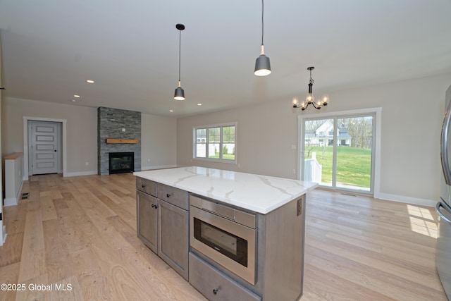 kitchen with light wood-type flooring, open floor plan, decorative light fixtures, and light stone countertops