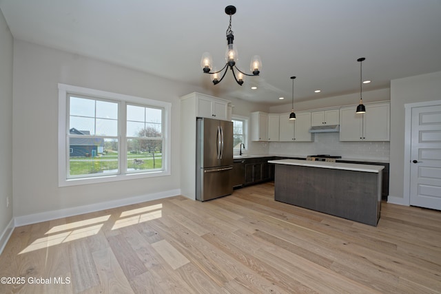 kitchen with backsplash, under cabinet range hood, light countertops, a notable chandelier, and stainless steel appliances