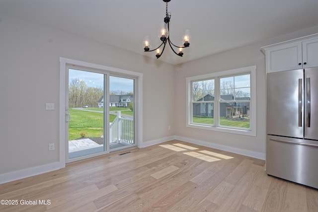 unfurnished dining area featuring baseboards, an inviting chandelier, and light wood-type flooring