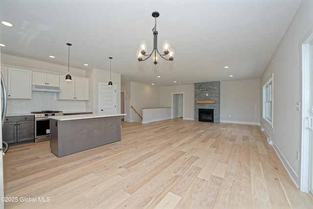 kitchen with decorative backsplash, gas range, light countertops, light wood-style floors, and under cabinet range hood
