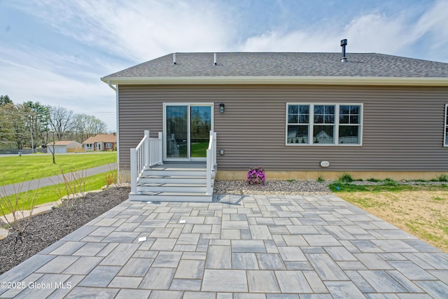 back of house featuring a lawn, roof with shingles, and a patio area