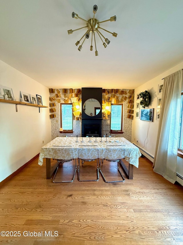 living area featuring wood finished floors, a wealth of natural light, baseboards, baseboard heating, and a notable chandelier