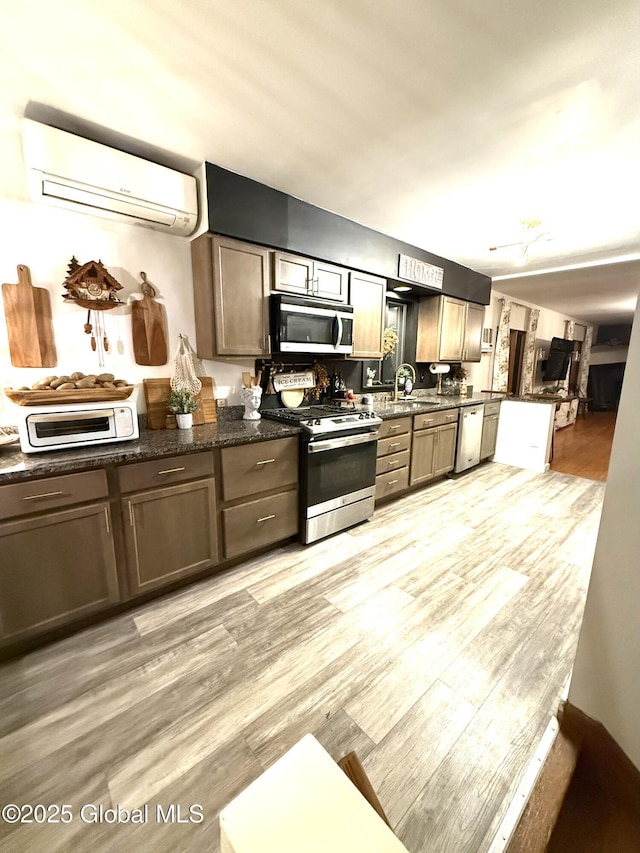 kitchen with a toaster, light wood-style floors, a wall mounted AC, a sink, and stainless steel appliances