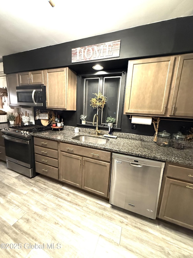 kitchen featuring a sink, dark stone countertops, stainless steel appliances, and light wood finished floors