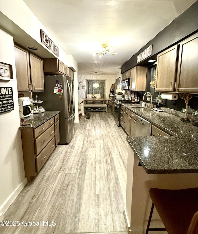 kitchen featuring appliances with stainless steel finishes, a sink, a peninsula, light wood finished floors, and dark stone counters
