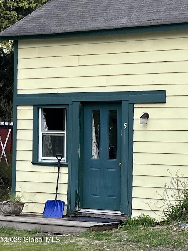 doorway to property featuring fence and a shingled roof
