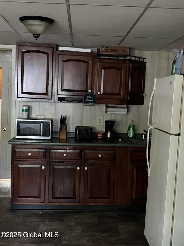 kitchen with freestanding refrigerator, a paneled ceiling, dark brown cabinetry, and dark countertops