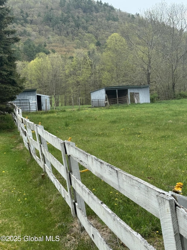 view of yard featuring a view of trees, fence, and an outbuilding