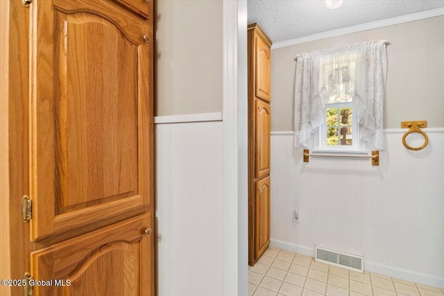 hall with visible vents, ornamental molding, a textured ceiling, a wainscoted wall, and light tile patterned floors