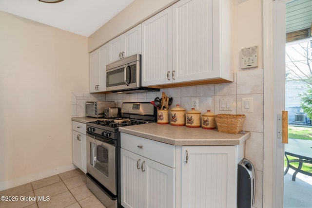 kitchen with backsplash, light tile patterned floors, light countertops, white cabinets, and stainless steel appliances