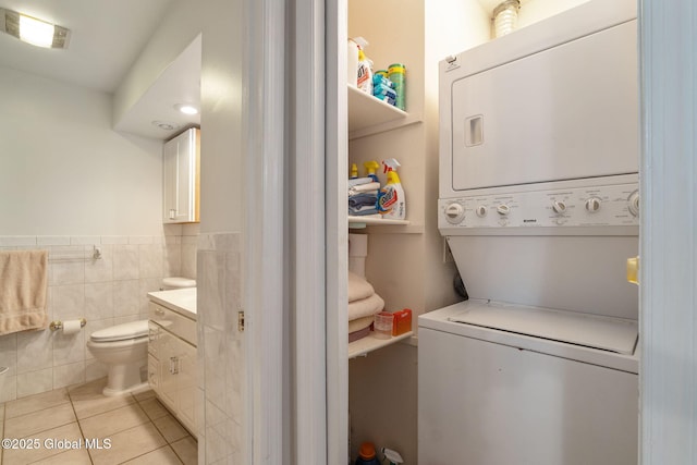 washroom featuring laundry area, visible vents, stacked washing maching and dryer, light tile patterned floors, and a wainscoted wall