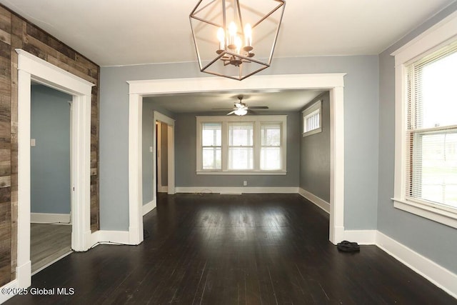unfurnished dining area featuring a chandelier, dark wood-type flooring, baseboards, and a ceiling fan