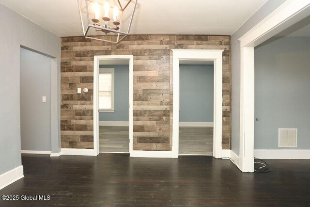 unfurnished dining area featuring a chandelier, wood finished floors, baseboards, and wood walls
