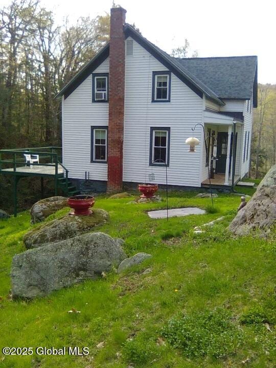 back of property featuring a shingled roof, a wooden deck, a yard, and a chimney