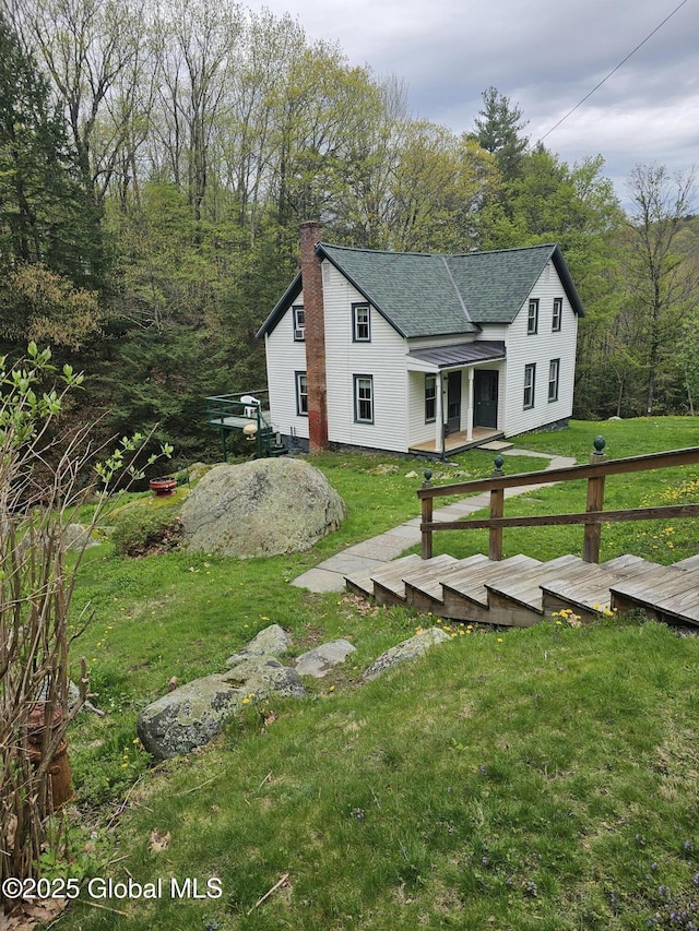 exterior space featuring a lawn, a shingled roof, a wooden deck, and a chimney
