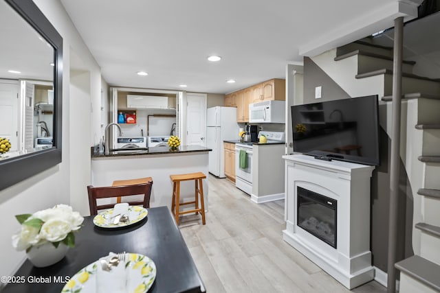 kitchen with a sink, white appliances, light wood-type flooring, recessed lighting, and dark countertops