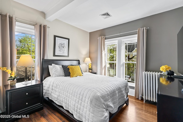 bedroom featuring beamed ceiling, radiator heating unit, visible vents, and dark wood-type flooring