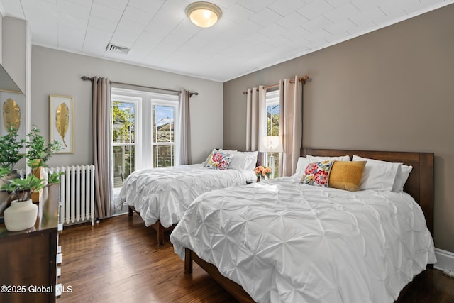 bedroom with radiator, visible vents, and wood finished floors