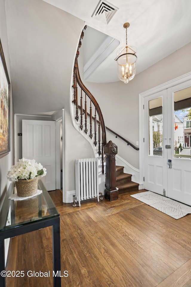 foyer featuring radiator, visible vents, stairs, a chandelier, and wood finished floors