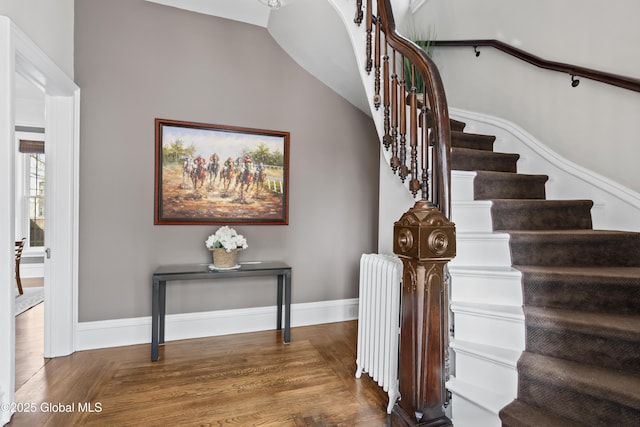 staircase featuring lofted ceiling, radiator, baseboards, and wood finished floors