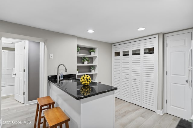 kitchen with a sink, a peninsula, a breakfast bar, open shelves, and light wood-style floors