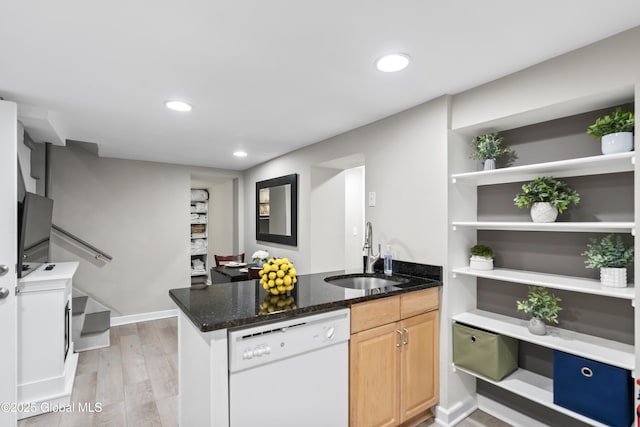 kitchen featuring a sink, a peninsula, dark stone counters, dishwasher, and light wood finished floors