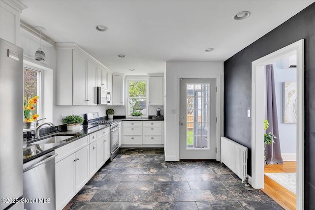kitchen with white cabinets, stainless steel appliances, a sink, and radiator heating unit