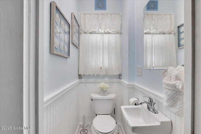 half bath with toilet, wainscoting, visible vents, and a sink
