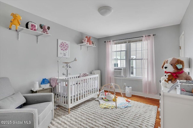 bedroom featuring cooling unit, a crib, and wood finished floors