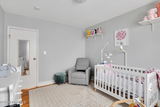 bedroom with a nursery area, baseboards, and wood finished floors