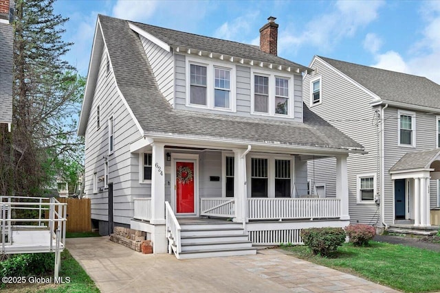 view of front facade with covered porch, roof with shingles, fence, and a chimney