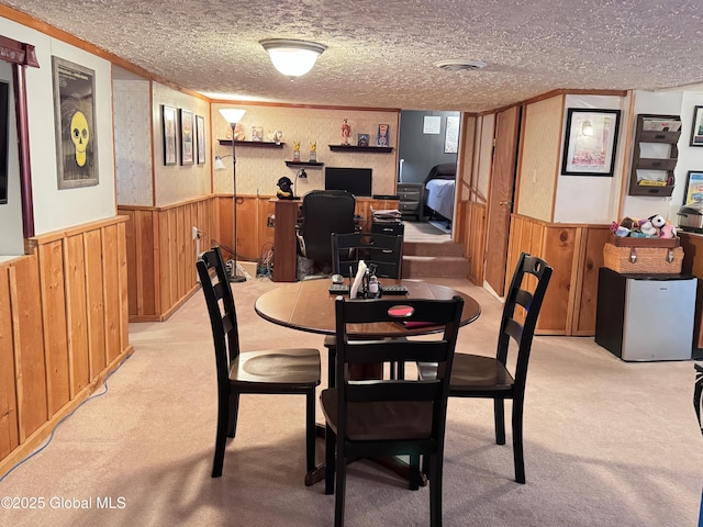 dining room with light colored carpet, a wainscoted wall, a textured ceiling, and wood walls