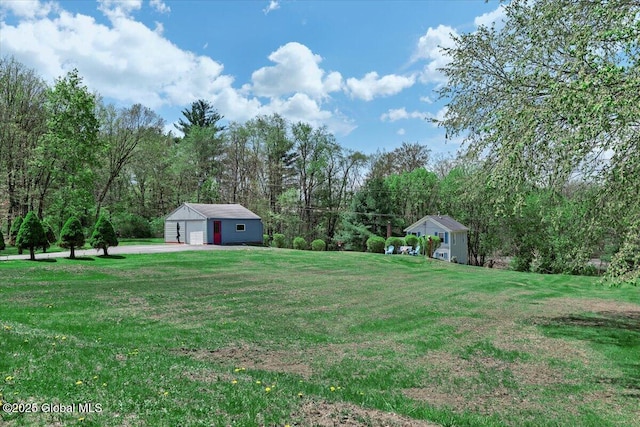 view of yard featuring an outdoor structure, a wooded view, and a detached garage