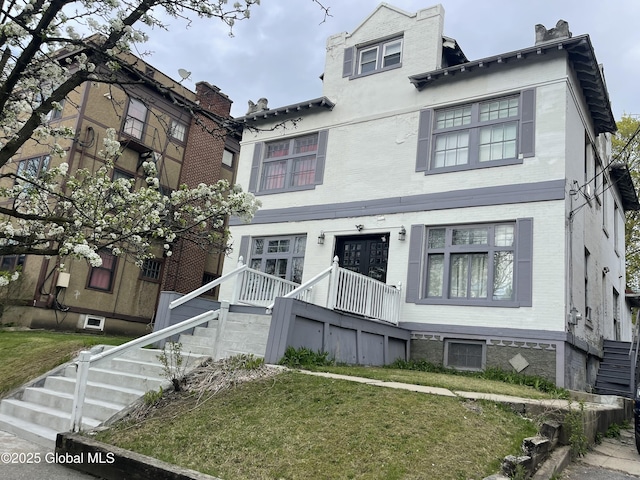 view of front facade featuring stairs, a front yard, and brick siding