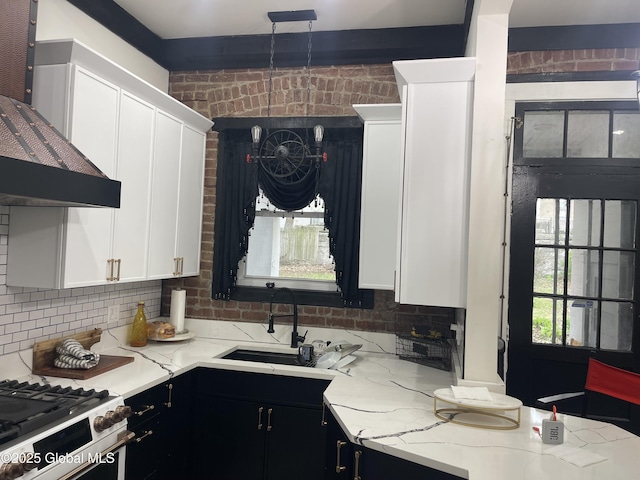 kitchen with a sink, dark cabinetry, wall chimney exhaust hood, white cabinetry, and light stone countertops