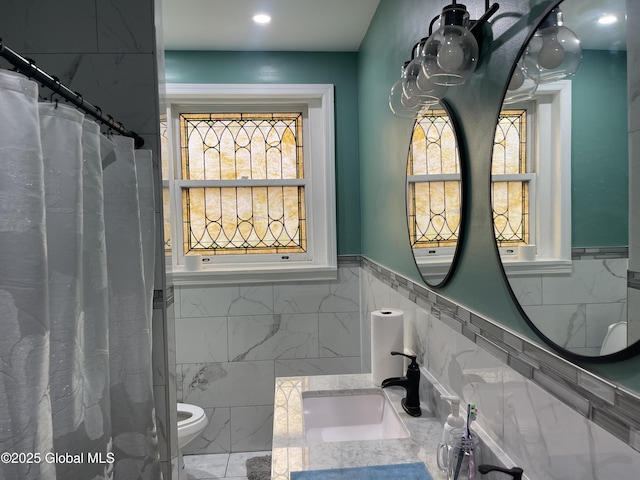 full bath featuring tile walls, a healthy amount of sunlight, wainscoting, and a sink