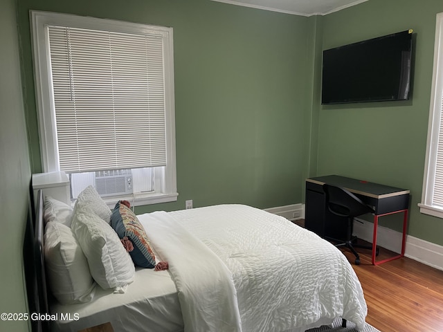 bedroom featuring cooling unit, wood finished floors, baseboards, and ornamental molding