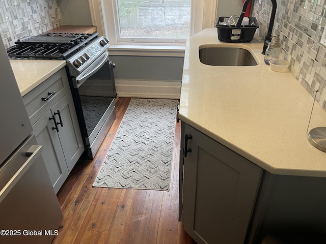 kitchen featuring stainless steel range with gas cooktop, hardwood / wood-style floors, decorative backsplash, and gray cabinets
