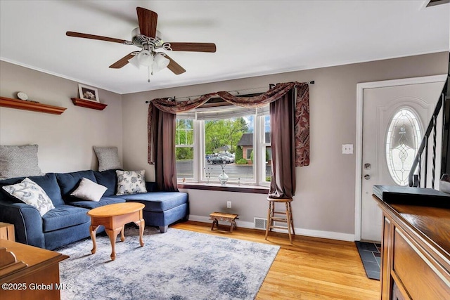 living area featuring a ceiling fan, light wood finished floors, baseboards, and ornamental molding