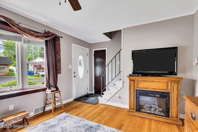 entrance foyer featuring light wood-style flooring, stairway, baseboards, a ceiling fan, and a glass covered fireplace