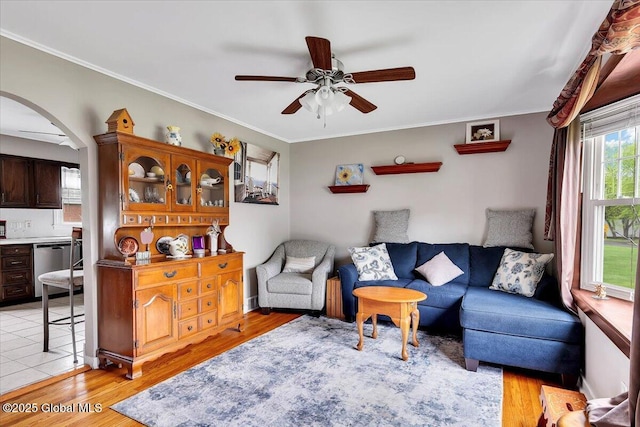 living area with a ceiling fan, arched walkways, light wood-style flooring, and crown molding