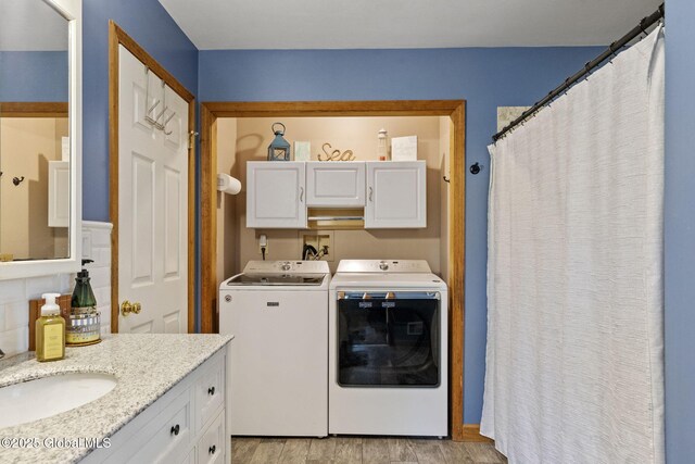 clothes washing area with washer and dryer, cabinet space, and light wood-style flooring